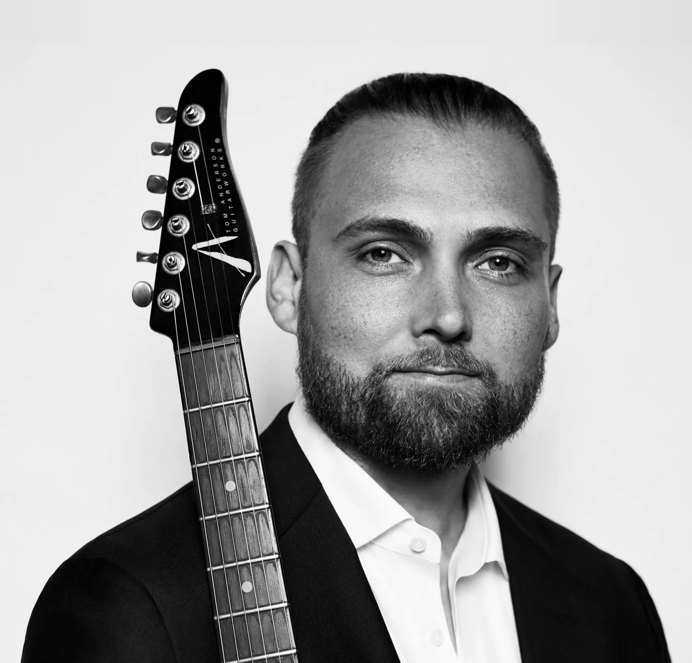 Black and white portrait of Joseph Daniel in a suit with an electric guitar neck beside him