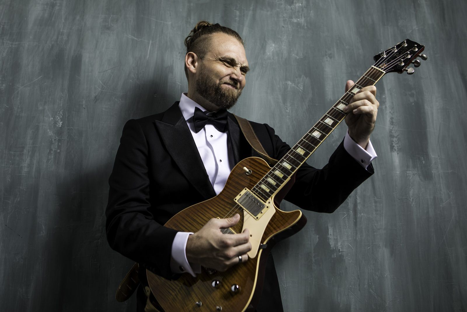 Joseph Daniel in a tuxedo playing an electric guitar with a broad grin